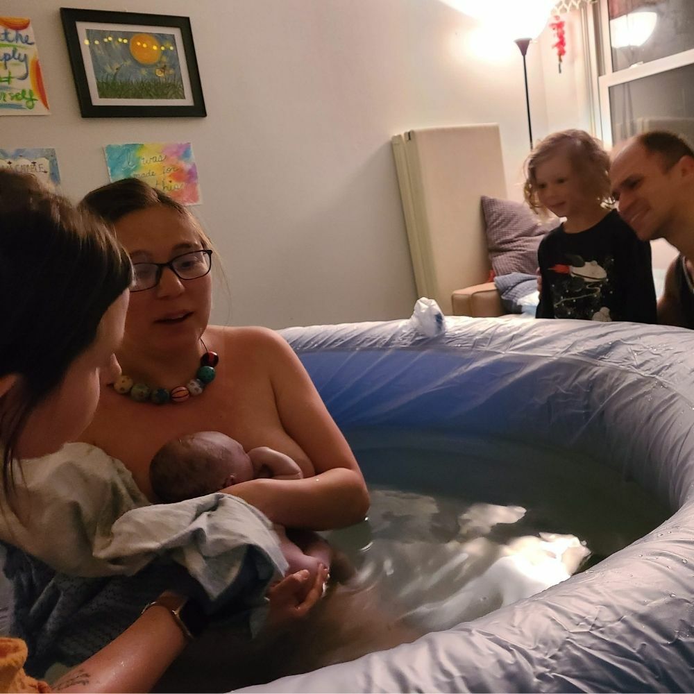 woman holding baby after a waterbirth at home with husband and daughter watching